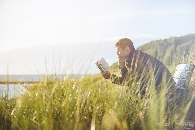 Photo of a man reading on a bench near a lake.