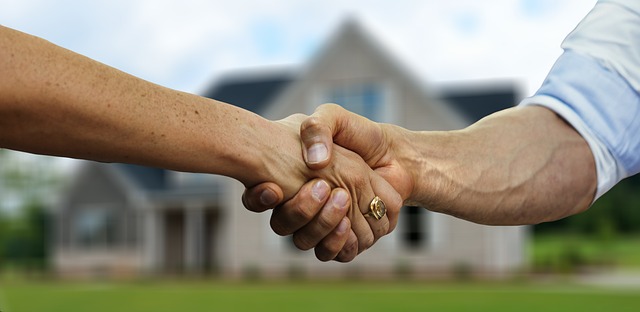 Two people shaking hands in front of a house.