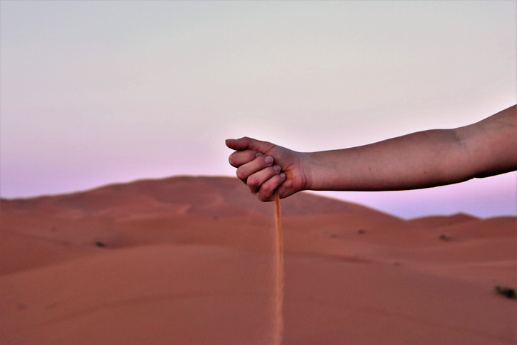 Woman dropping sand into Sahara Desert with dune in background.
