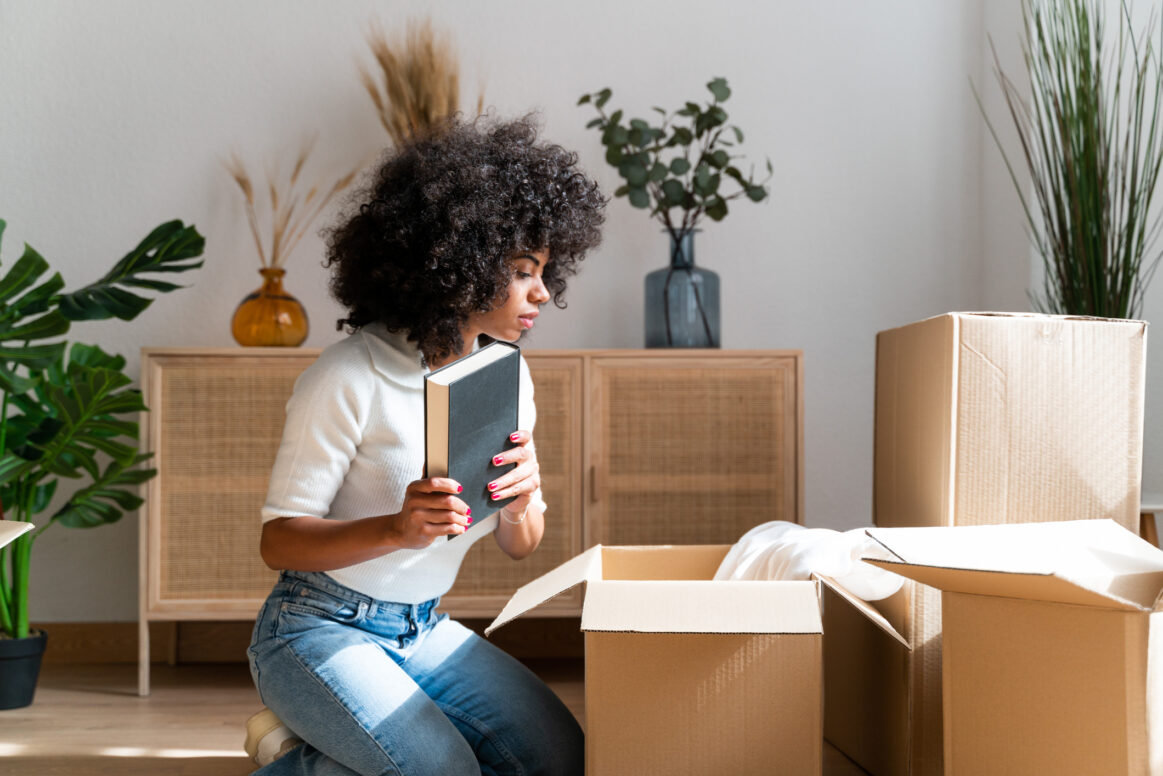 Brown woman with beautiful afro unpacking her favorite books in her new home.