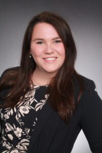 Young, smiling white woman with long brown hair in a black suit