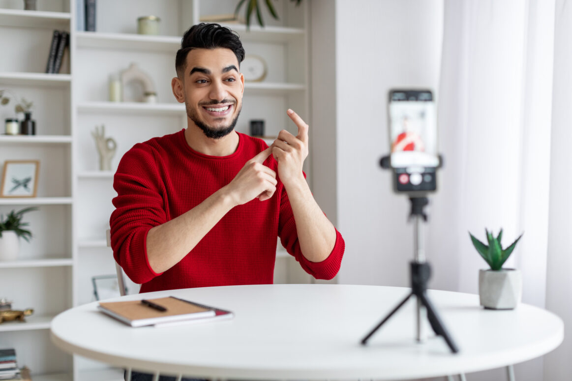 Young brown blogger recording content for social media using his smartphone and a tripod.