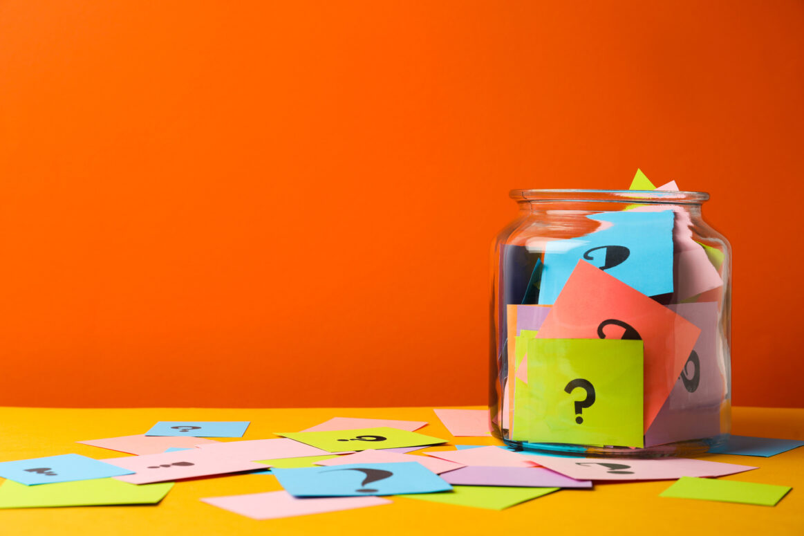 Colorful cards with question marks in glass jar on orange background.