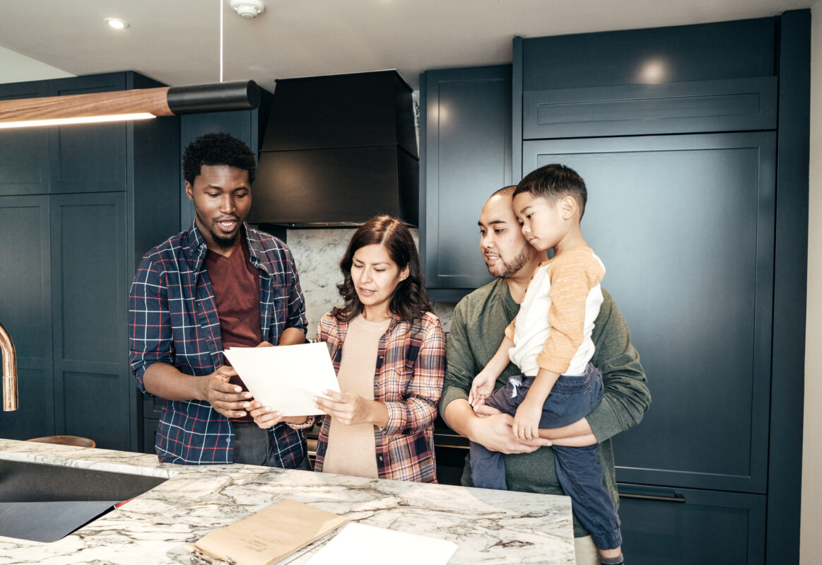 Multifacial family with two children standing in kitchen talking with real estate professional