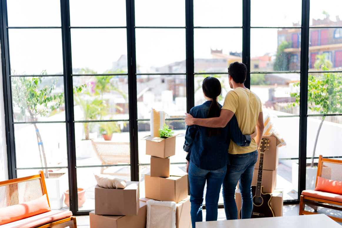 Rear view of a young couple looking through window at the new house