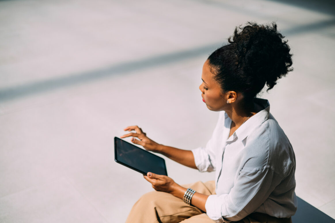 A high angle view of a serious Latin entrepreneur scrolling on her tablet while sitting on the street bench.