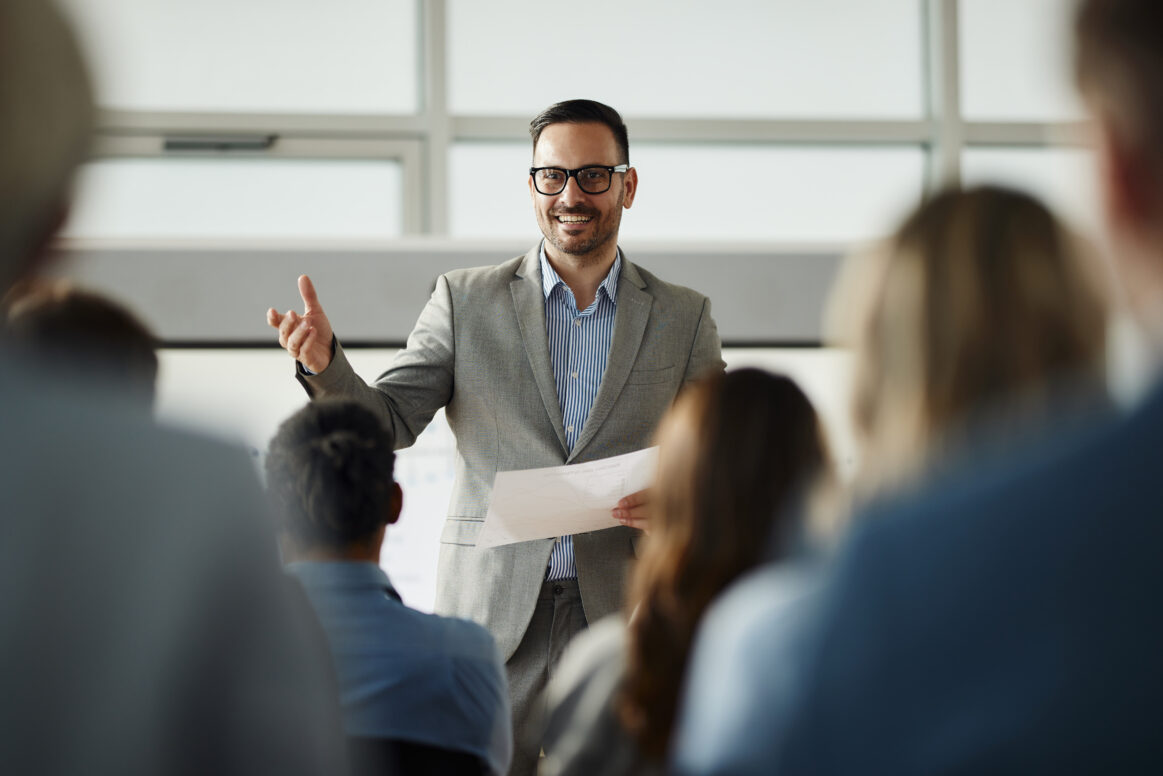 Happy business leader talking to his colleagues during an education event in board room.