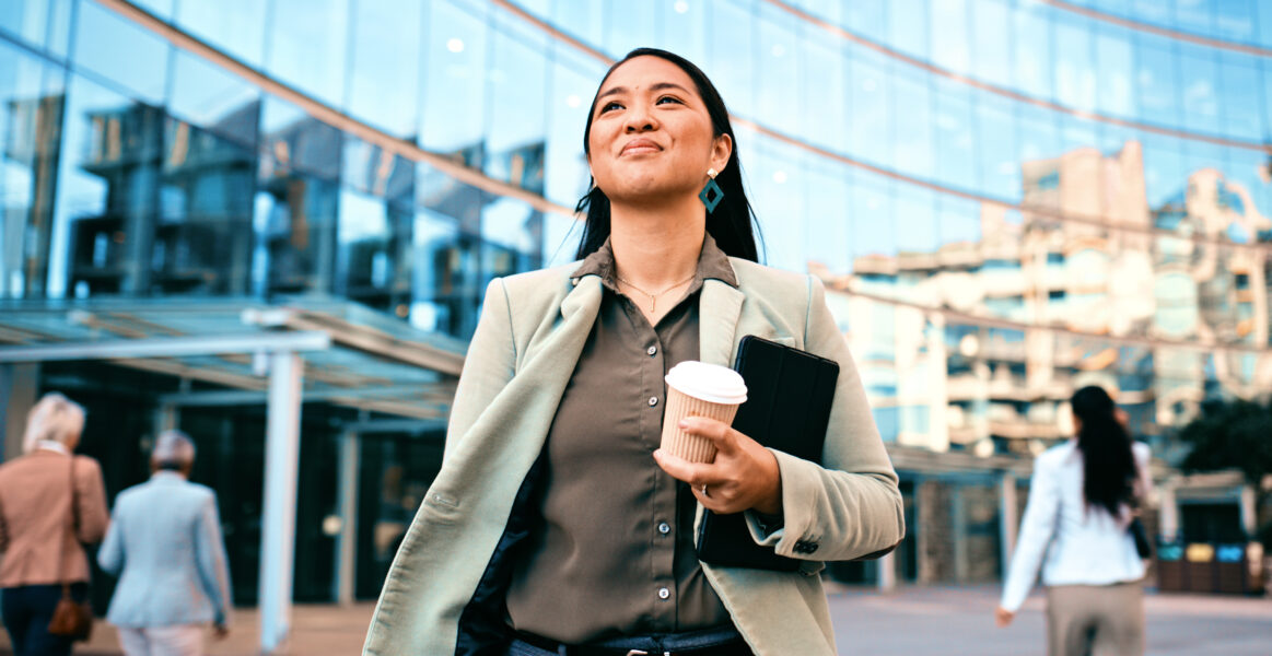 Smiling businesswoman holding coffee and documents while walking outside a modern office building. Corporate environment, confidence, and urban lifestyle.